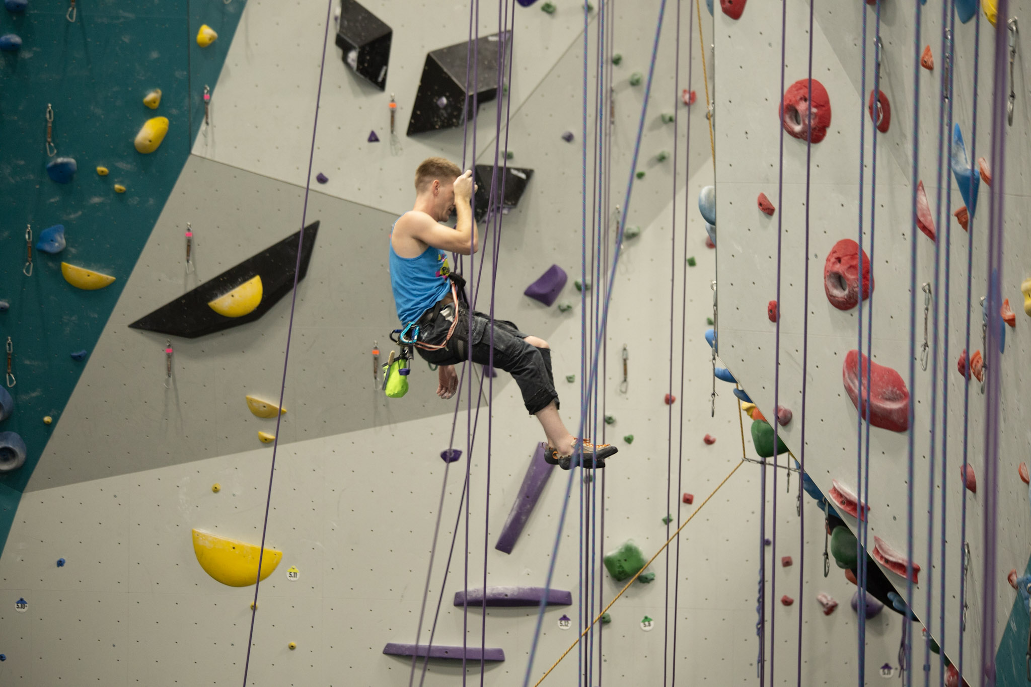 Climber in a blue tank top working up a rope route at Send It Climbing Gym